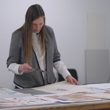 A woman leans over a bench of large sketches